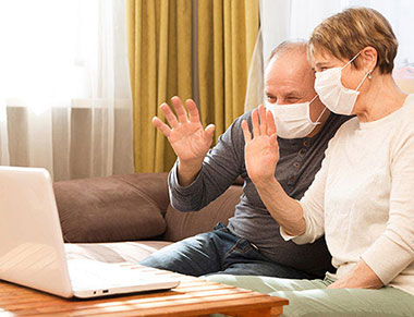Older couple wearing masks and waving to a laptop.