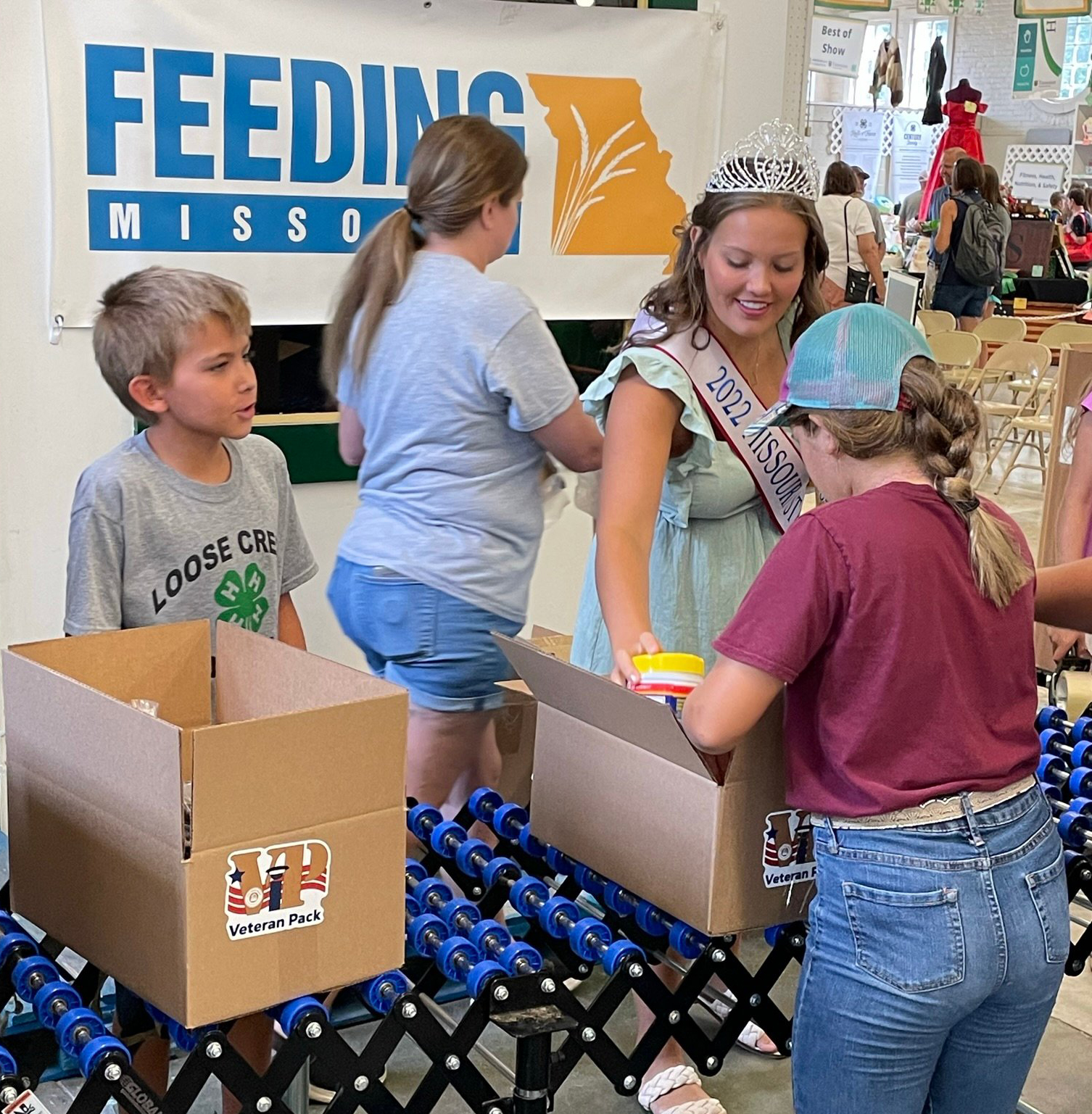 Open 2022 Missouri State Fair Queen Elsie Kigar assists with packing boxes of meals for veterans during the 4-H Feeding Missouri event at the fair.