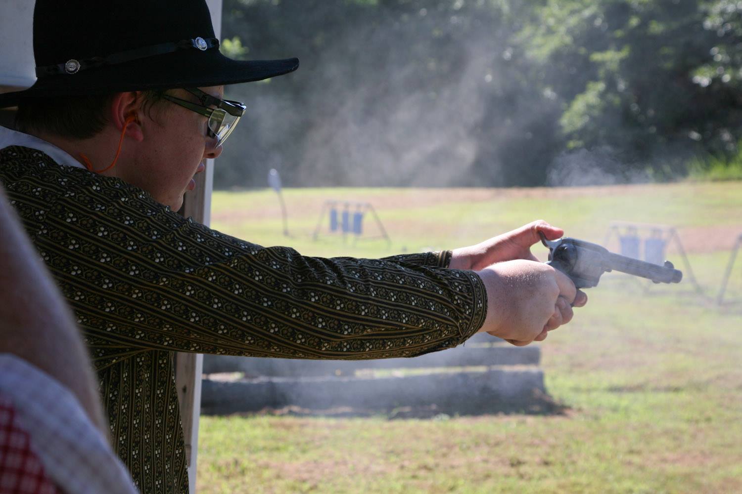 Young boy firing a rimfire pistol at an outdoor shooting range.