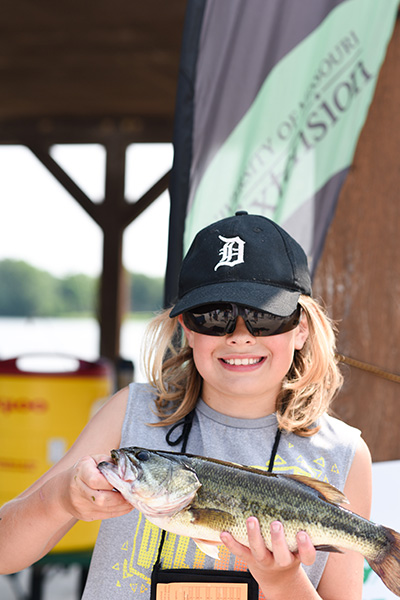 A young girl smiles to the camera while holding a fish she caught.