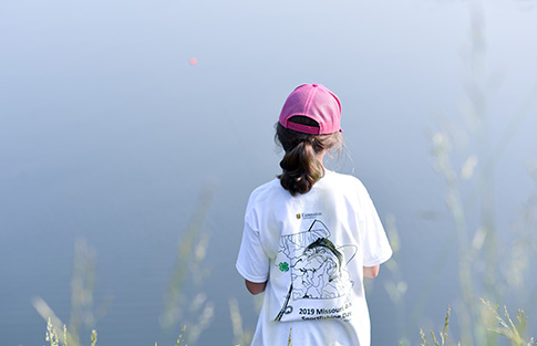 A young girl looks over a lake while fishing.