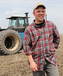 A young farmer in a field standing in front of a tractor.