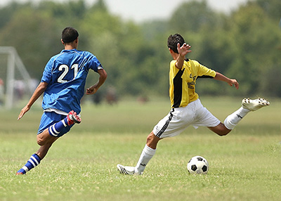 Two uniformed boys on opposite teams playing soccer in a field