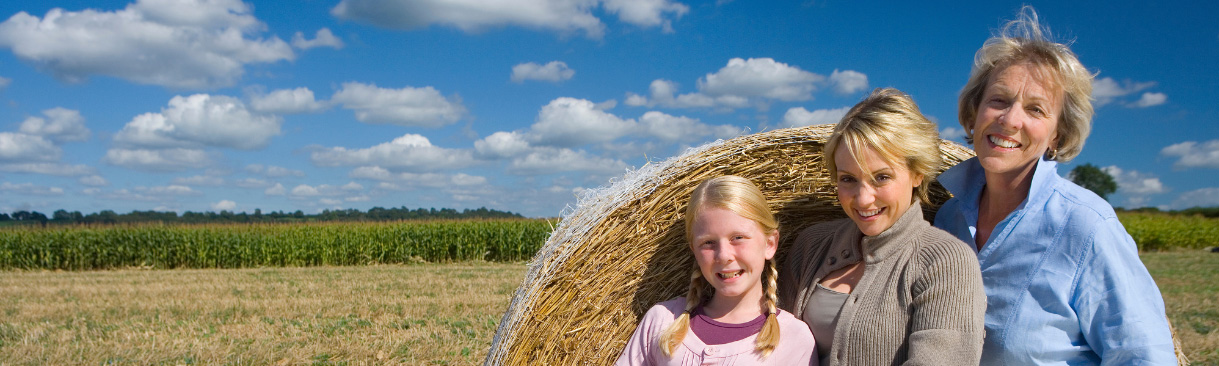 A mother, daughter and granddaughter standing in front of a hay bale in a field