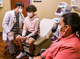 Doctor listening to chest of teen patient in exam room