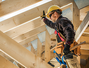 A construction worker standing inside roof trusses being built.