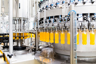 Drink bottles being filled with an orange beverage in a packing plant.