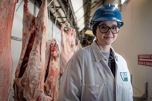 Smiling woman in lab coat and hard hat in meat factory