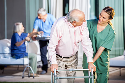 A nurse helps an elderly man with his walker.