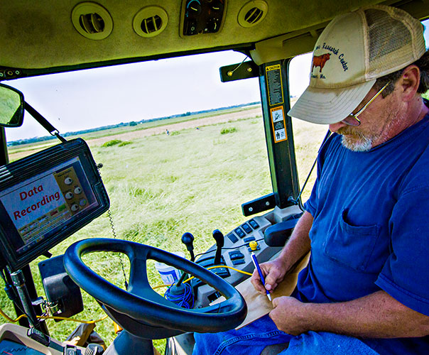 Stacey Hamilton takes notes while measuring forage density from the cab of a harvester in a field.