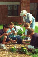 An adult leader working with kids in a garden plot