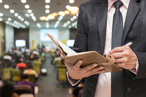 Businessman using a tablet in a seminar room with attendees in the background.