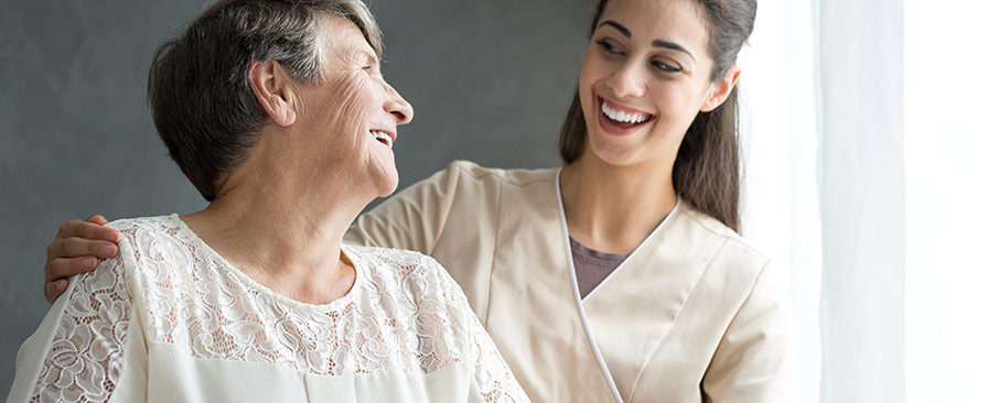 Young female caregiver happily helping elderly woman