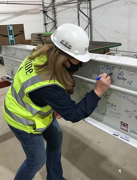 Jennifer Hart in hardhat and high-visibility vest signing a construction beam. Image property of Hartline Construction. Used with permission.