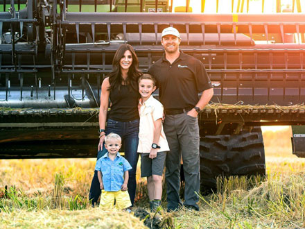 Sam Schneider and his wife and two young sons standing in a rice field in front of a rice harvester.