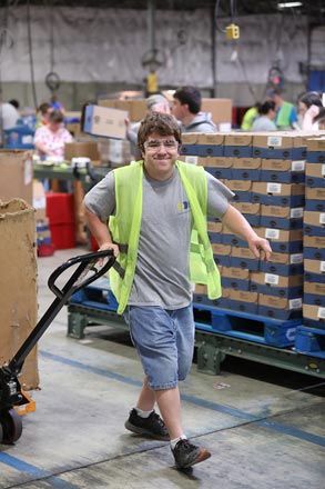 A man pulling a pallet containing a large box through a warehouse.