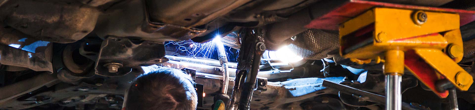 A mechanic welding a part on the underside of a car.