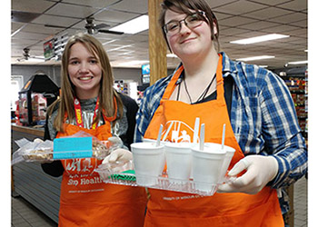 Two girls in aprons providing free samples at a grocery store.