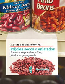 A Spanish-language shelf talker on the canned bean shelf extolling the high protein and fiber, and low fat and sodium in dried or canned beans.