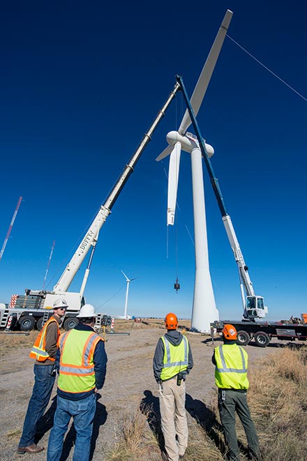 Four men at a wide turbine construction site.