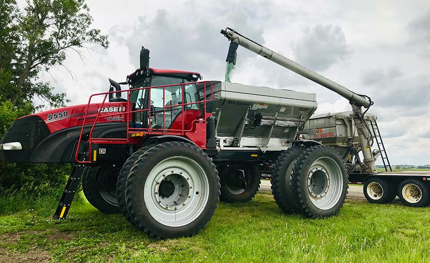 A high-clearance spinner spreader being refilled with a mixture of fertilizer and a cover crop seed mix.