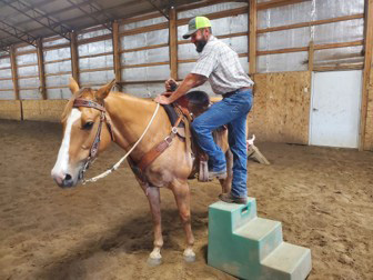 A man using a mount block to get on a horse.
