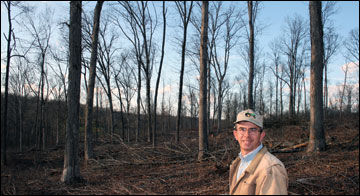 A man standing in a woodland of bare trees.