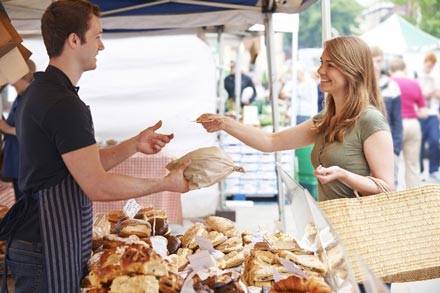 A woman buying bread from a man at a farmers market booth.