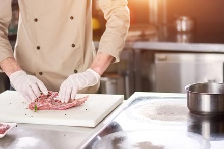 A chef standing at a kitchen counter manipulating meat on a cutting board.