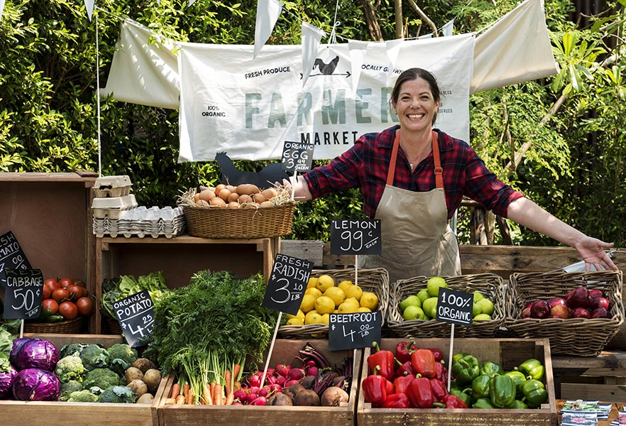 Farmers market stand with a woman showcasing her products.