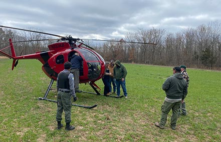 Ground crew surrounds a helicoptor prior to take-off for aerial operations for feral hog elimination.