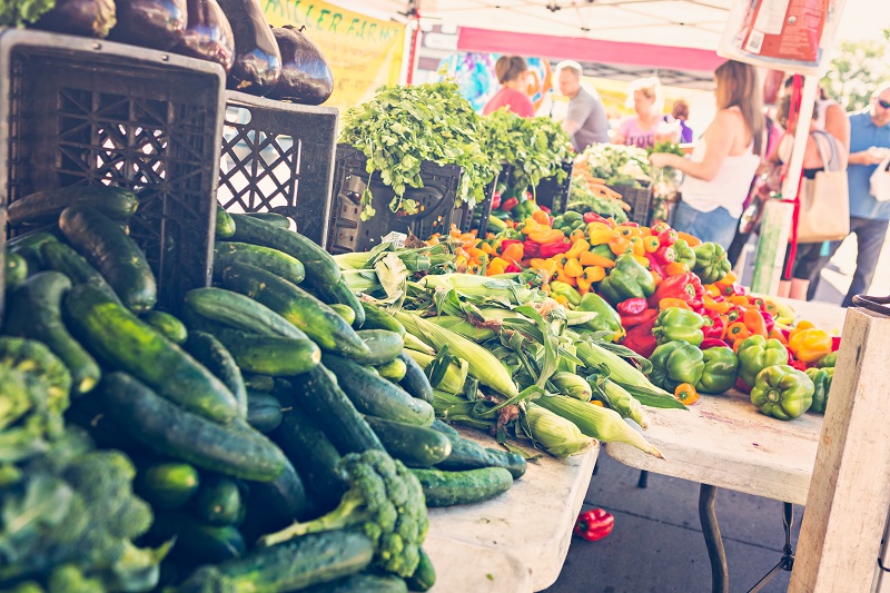 Cucumbers, corn and peppers on a table in a farmers market stall.