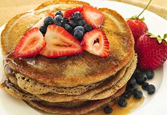 A stack of pancakes topped by strawberries, blueberries and syrup.