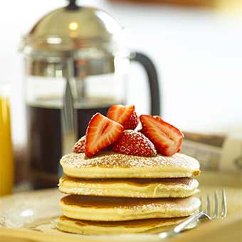 Pancakes topped by strawberries, with coffee and orange juice in the background.