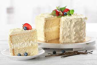 A vanilla cake on a platter with one slice removed and sitting on a plate.