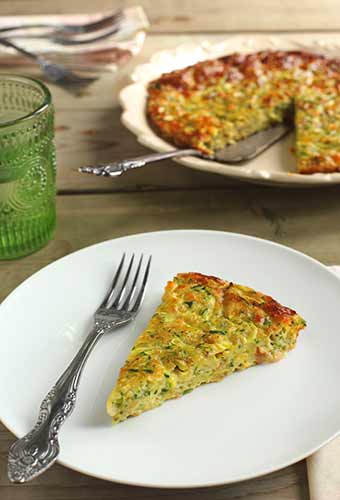 A pan of quiche with one sliced removed and sitting on a plate with a fork.