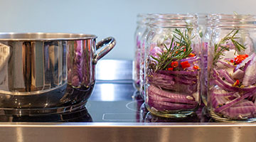 A pot on a stove next to mason jars with onions inside.