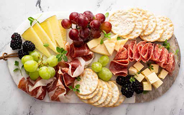 a cutting board with various meats, cheeses, fruits and crackers