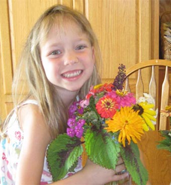 Smiling young girl holding a vase of flowers.