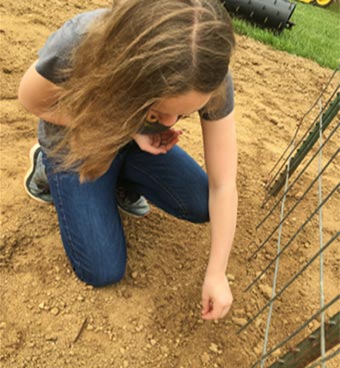 A young girl on her knees planting seeds in a garden.