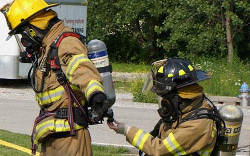 One firefighter checking another firefighter's equipment.