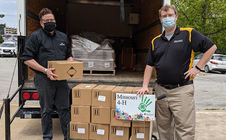 Two men wearing masks handing out boxes of hand sanitizer.