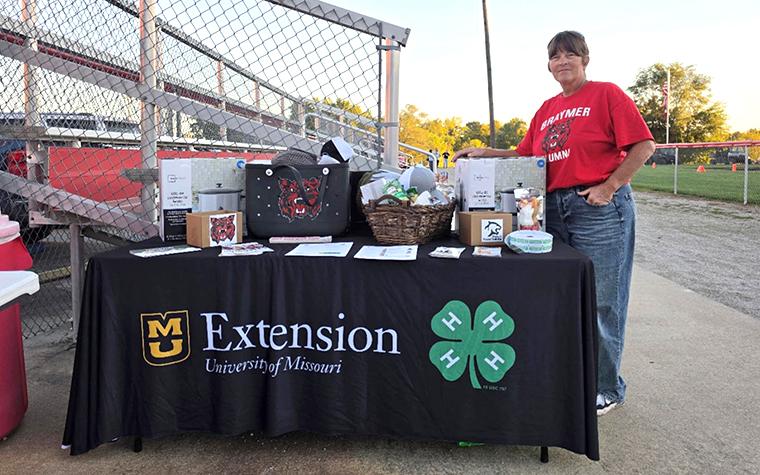 Woman standing next to table with MU Extension branding and covered with donated gift items