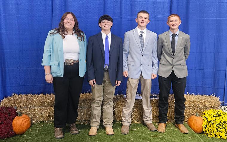 Four youths lined up amidst hay bales and pumpkins against a background of blue drapery