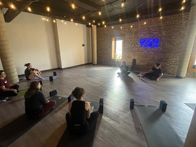 Instructors and class participants seated on yoga mats in Moon Yoga studio.