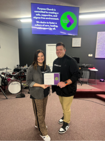 Ashley and Josh Harrison in Purpose Church smiling and holding their RFW certificate standing under RFW banner.
