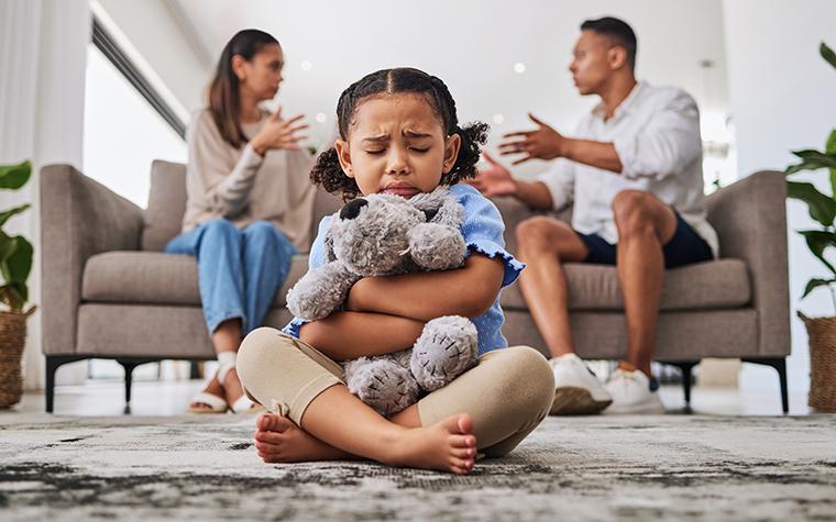 Upset child holding stuffed animal while parents argue in background