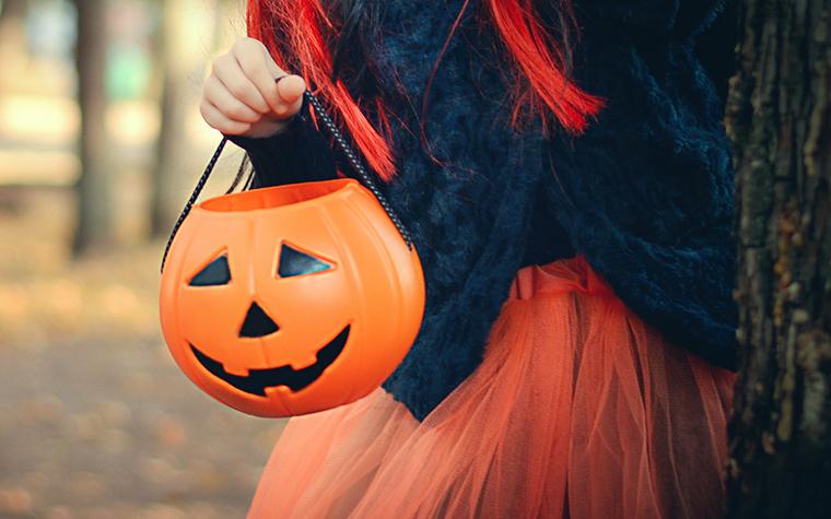 Close-up of children with pumpkins bags playing trick or treat outdoors.