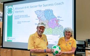 A man and woman hold a soccer ball in front of a projector screen.