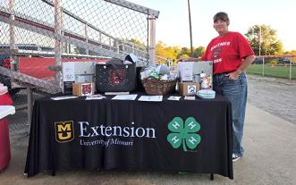 Woman standing next to table with MU Extension branding and covered with donated gift items